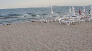 Une plage avec des chaises longues blanches et des parasols, un rivage sablonneux et une mer calme.