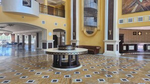 Un hall d’entrée spacieux, doté d’un sol en marbre, d’une table ronde centrale et d’un plafond haut orné d’éléments décoratifs.