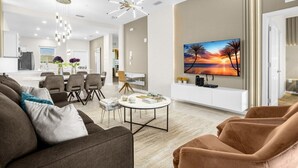 Moderni olohuone, jossa on suuri litteänäyttöinen televisio, ruokailutila tuoleineen sekä taustalla keittiö.