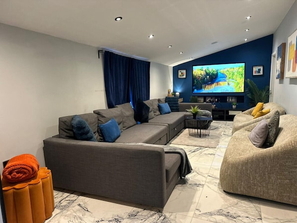A modern living room with a sectional sofa, a round coffee table, and a flat-screen TV mounted on the wall.