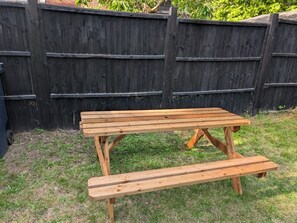 A wooden picnic table with benches, set against a wooden fence.