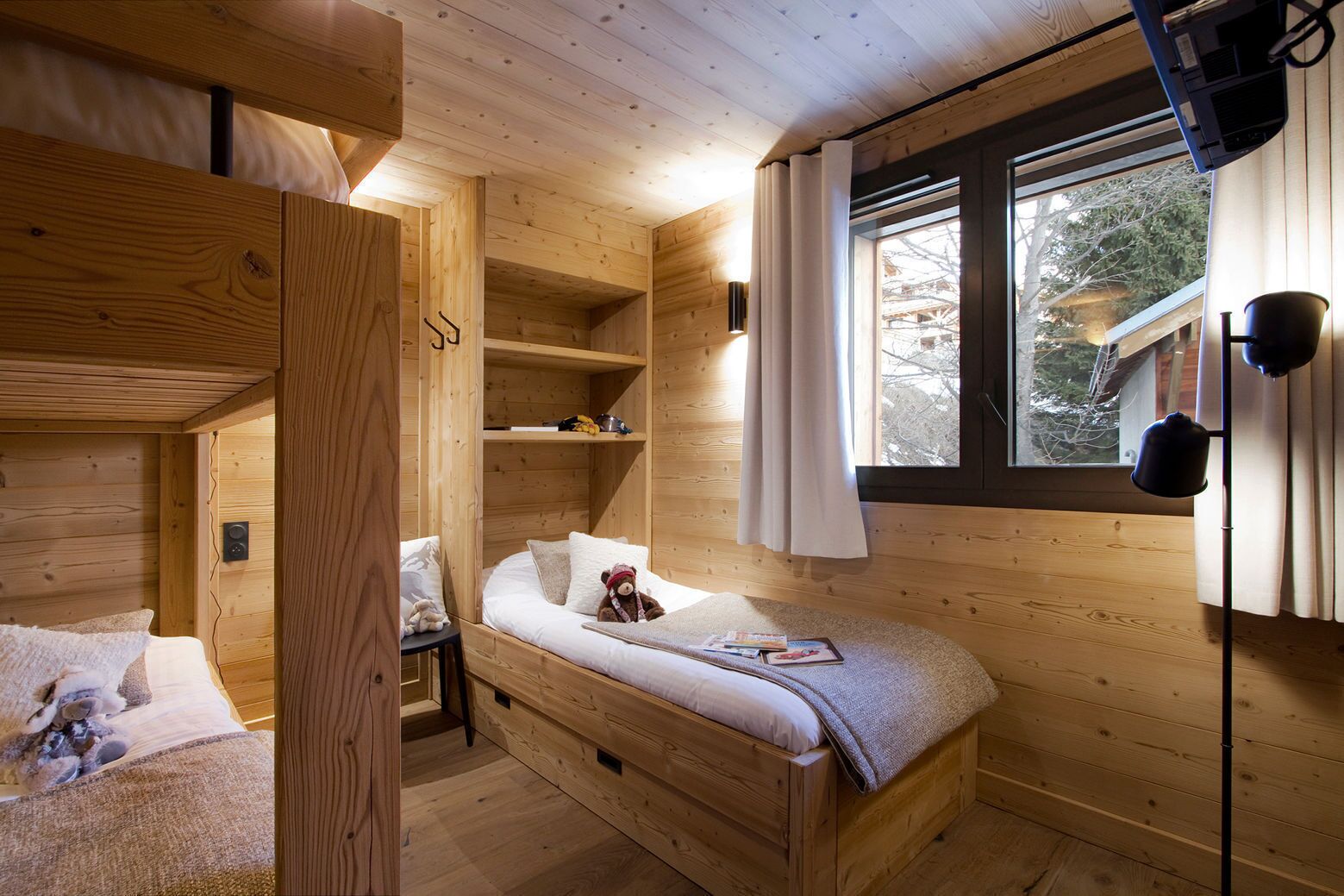 Een gezellig houten kamer met stapelbedden, een klein tafeltje en een raam met gordijnen.