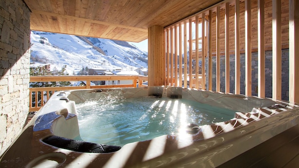 Un jacuzzi con interior de madera, una pared de piedra y vistas a montañas nevadas.