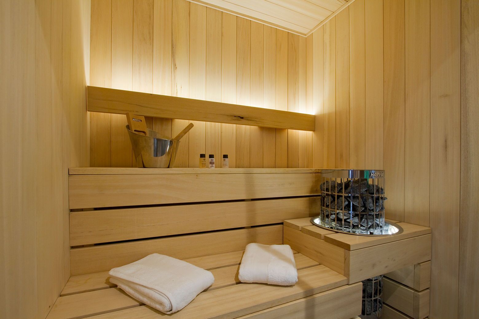 Un sauna en bois avec un banc, une étagère avec des bouteilles et un récipient en verre contenant des pierres.