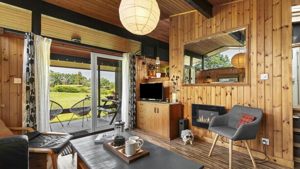 Een gezellig chalet interieur met een houten gevel, een open haard, een televisie en een eethoek met een tafel en stoelen.