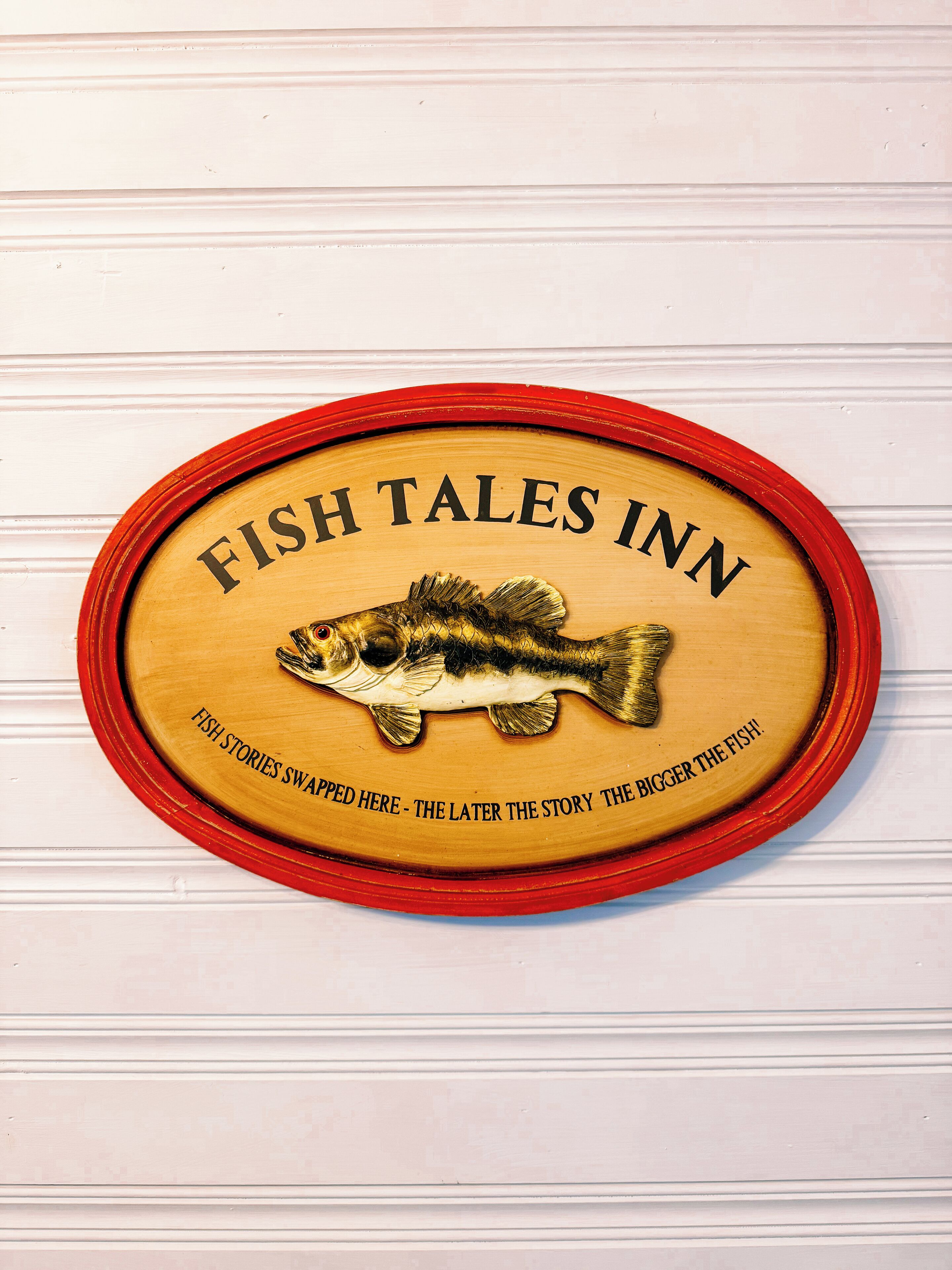 Eine Holztafel mit einer Fischillustration und dem Text 'FISH TALES INN' und 'HIER WERDEN FISCHGESCHICHTEN ERZÄHLT – JEDERZEIT GANZ GROSSE.'