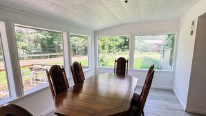 A spacious dining room with a large wooden table and six chairs, large windows offering a view of the outdoors, and a ceiling with a textured finish. - Charming 2-bedroom house in wonderful Bristol located on the Aplachicola River (Bristol)
