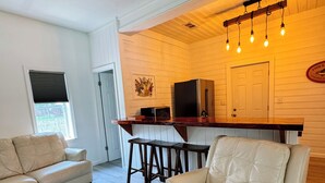 A spacious living room with a beige sofa, a round rug, and a kitchen area with a refrigerator, a TV, and a wooden dining table. - Charming 2-bedroom house in wonderful Bristol located on the Aplachicola River (Bristol)