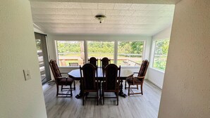 A dining area with a table and four chairs, large windows with a view of greenery, and a ceiling fan. - Charming 2-bedroom house in wonderful Bristol located on the Aplachicola River (Bristol)