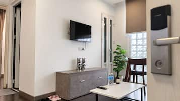A modern room with a flat-screen TV mounted on the wall, a grey cabinet, a small table with a remote control, a potted plant, and a wooden chair.
