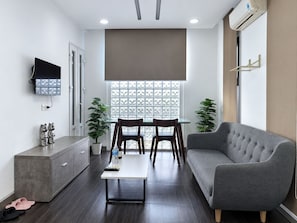 Una sala de estar moderna con un sofá gris, una mesa de comedor con sillas, un televisor montado en la pared y un amplio ventanal con vistas.