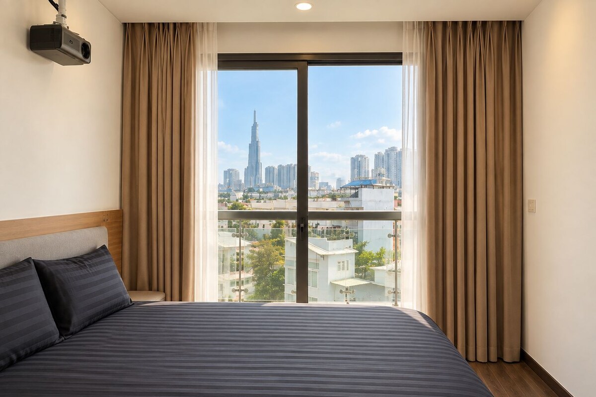 Une chambre d’hôtel avec un grand lit, un projecteur fixé au mur et une vue sur le paysage urbain, visible à travers une grande fenêtre.