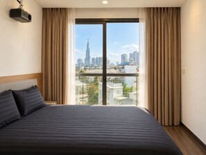 Une chambre d’hôtel avec un grand lit, un projecteur fixé au mur et une vue sur le paysage urbain, visible à travers une grande fenêtre.