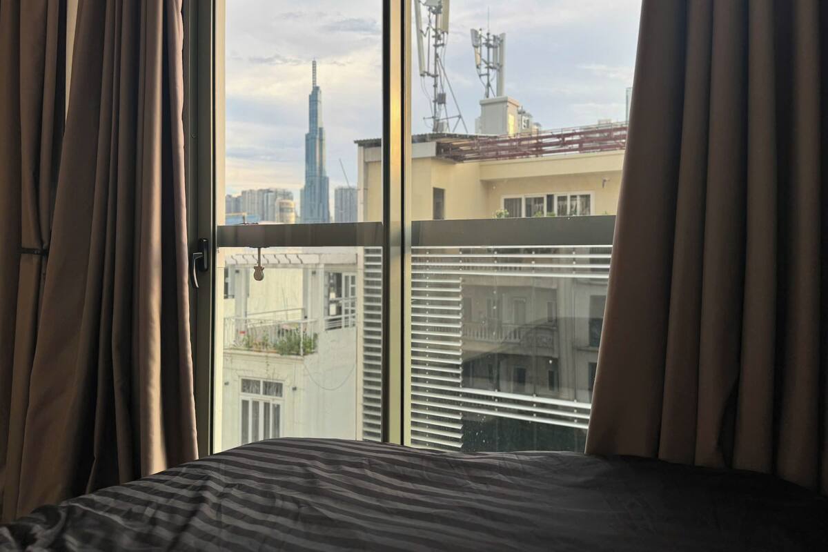 A bedroom with a large window overlooking a cityscape, including a tall building and communication towers.