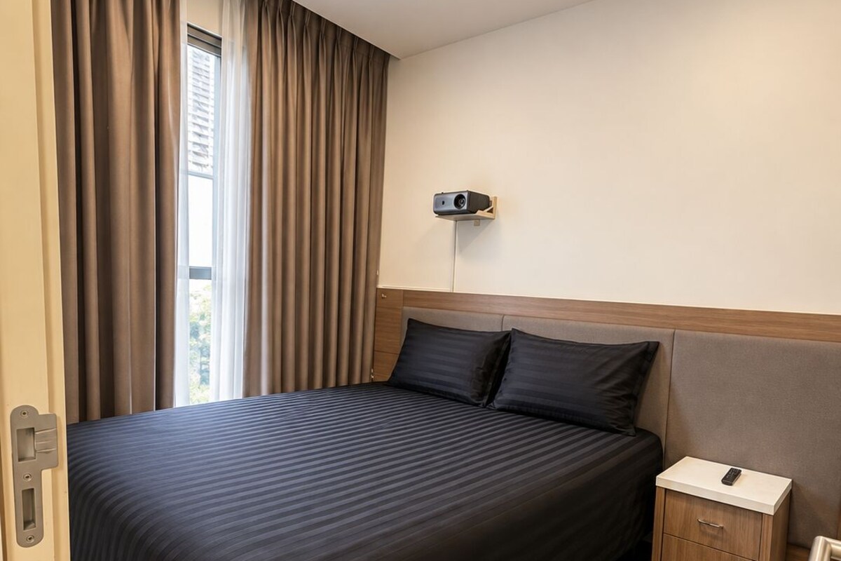 Une chambre d’hôtel avec un grand lit, une table de chevet avec une télécommande et un projecteur fixé au mur.