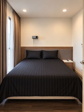 A hotel room with a large bed, a bedside table, a wall-mounted projector, and a window with curtains. - Uhouse - MELIA Thao Dien Hotel & Apartment (Ho Chi Minh City)