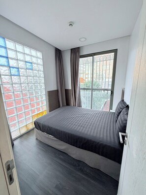 A bedroom with a large bed, a window with curtains, a ceiling light, and a view of buildings outside. - Uhouse - MELIA Thao Dien Hotel & Apartment (Ho Chi Minh City)