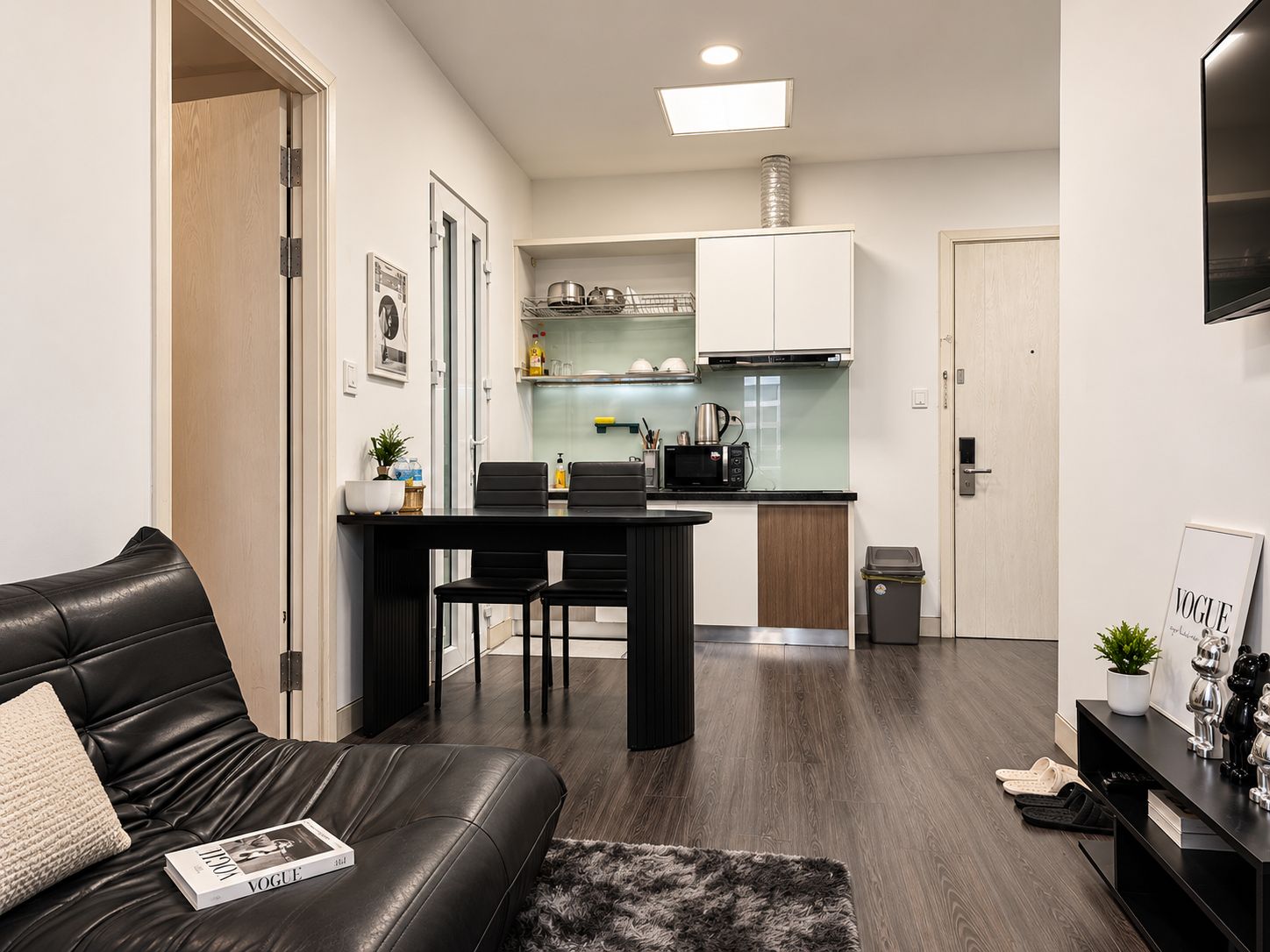 Un espacio habitable compacto con sofá, una mesa de comedor con sillas, una cocina con armarios y electrodomésticos, y un televisor montado en la pared.