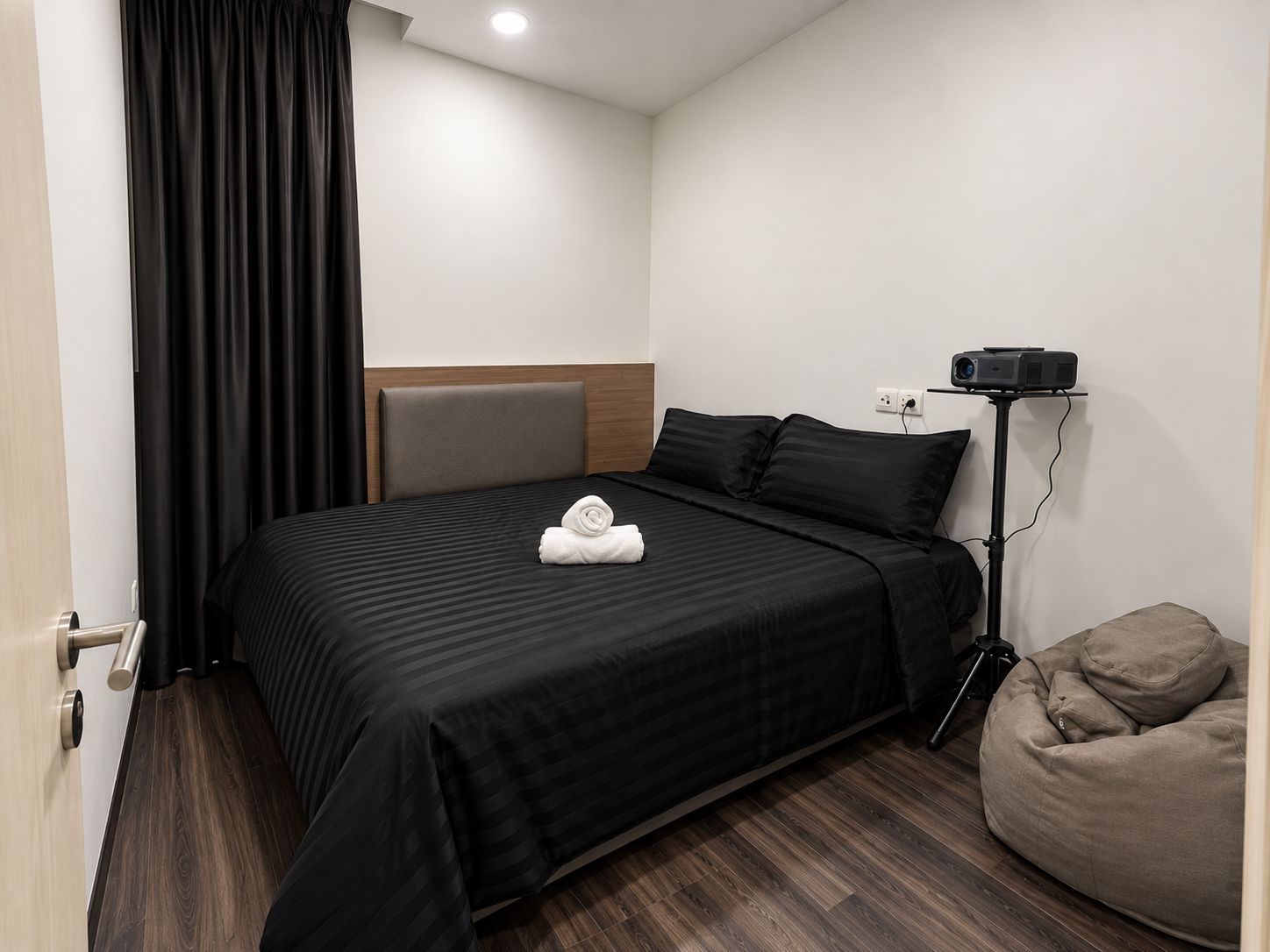 A hotel room with a bed, a projector, a bean bag, and a door.