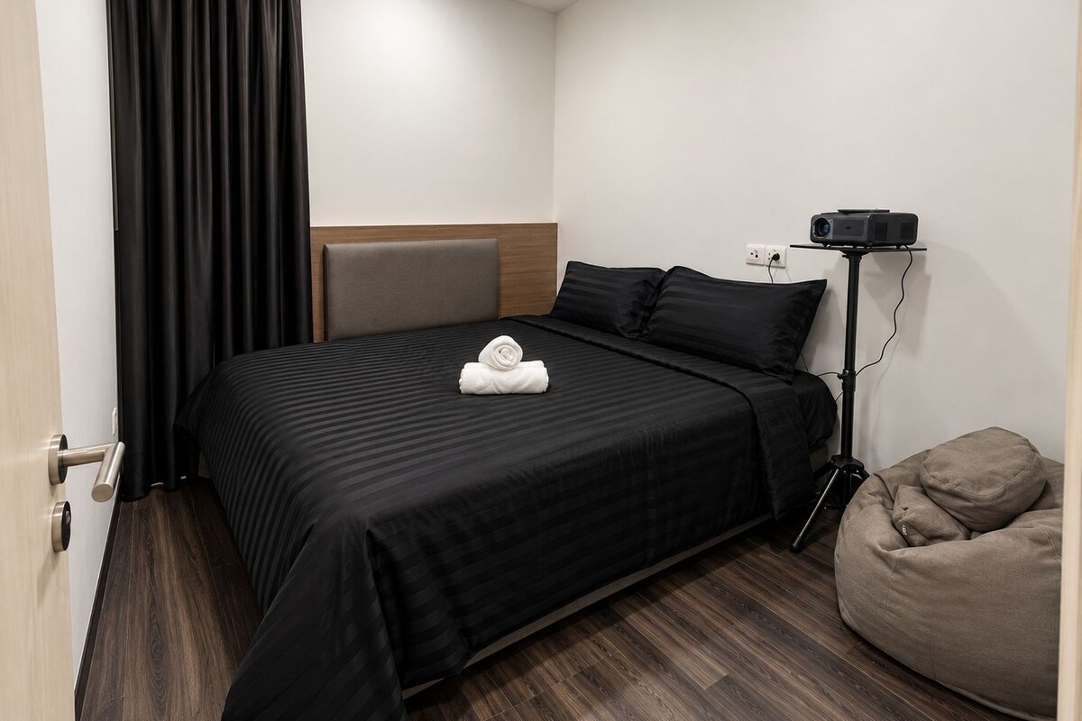 Une chambre d’hôtel avec un lit, un projecteur, un fauteuil poire et une porte.