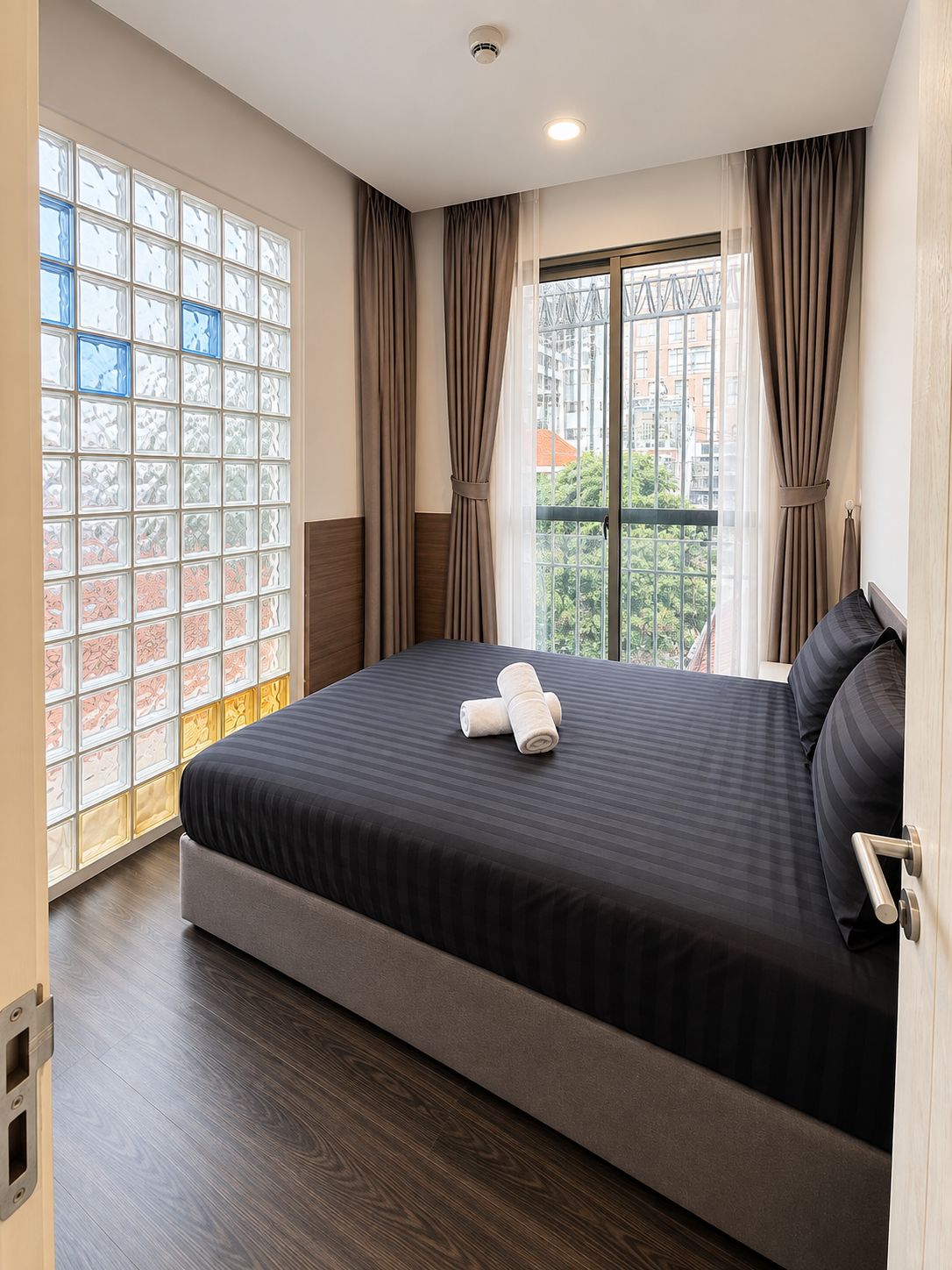 A hotel room with a large bed, a window with curtains, and a view of the cityscape.