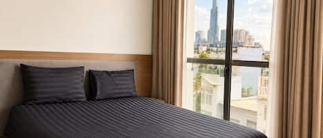 A hotel room with a large bed, a projector mounted on the wall, and a view of a city skyline through a large window.