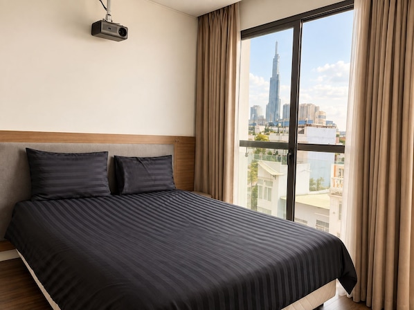 A hotel room with a large bed, a projector mounted on the wall, and a view of a city skyline through a large window.