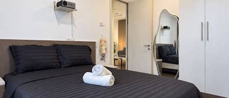 A hotel room with a bed, a mirror, a wardrobe, and an air conditioning unit.