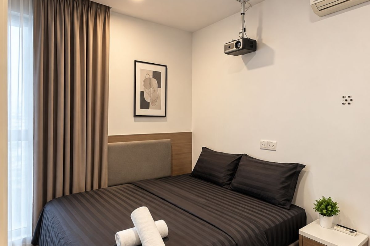 Une chambre d’hôtel avec un grand lit, une table de chevet agrémentée d’une plante, un climatiseur fixé au mur et un luminaire au plafond.