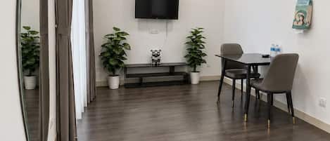 A modern living room with a flat-screen TV, a dining table with chairs, a bench, and potted plants.