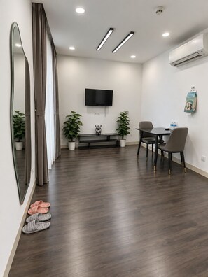 Uma sala de estar moderna com televisão de tela plana, uma mesa de jantar com cadeiras, um banco e plantas em vasos.