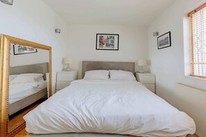 Een slaapkamer met een groot bed, twee nachtkastjes met lampen, een spiegel en twee ingelijste foto's aan de muur.