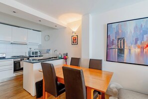 Een moderne keuken met witte kasten, een eettafel met stoelen, een magnetron en een spoelbak.