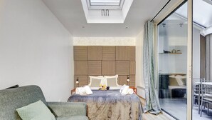 Une chambre d’hôtel moderne équipée d’un lit, d’un canapé, d’une porte vitrée donnant sur un balcon et d’une lucarne au-dessus du lit.