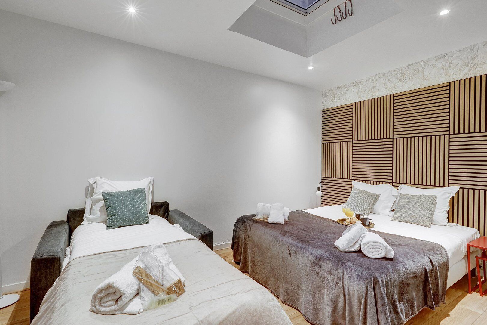 A hotel room with two beds, each with a pillow, a bedside table, and a towel on the bed.