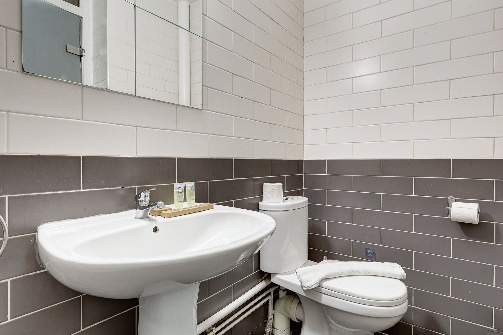 Een badkamer met een wit wastafel, toilet en grijze betegelde wanden.