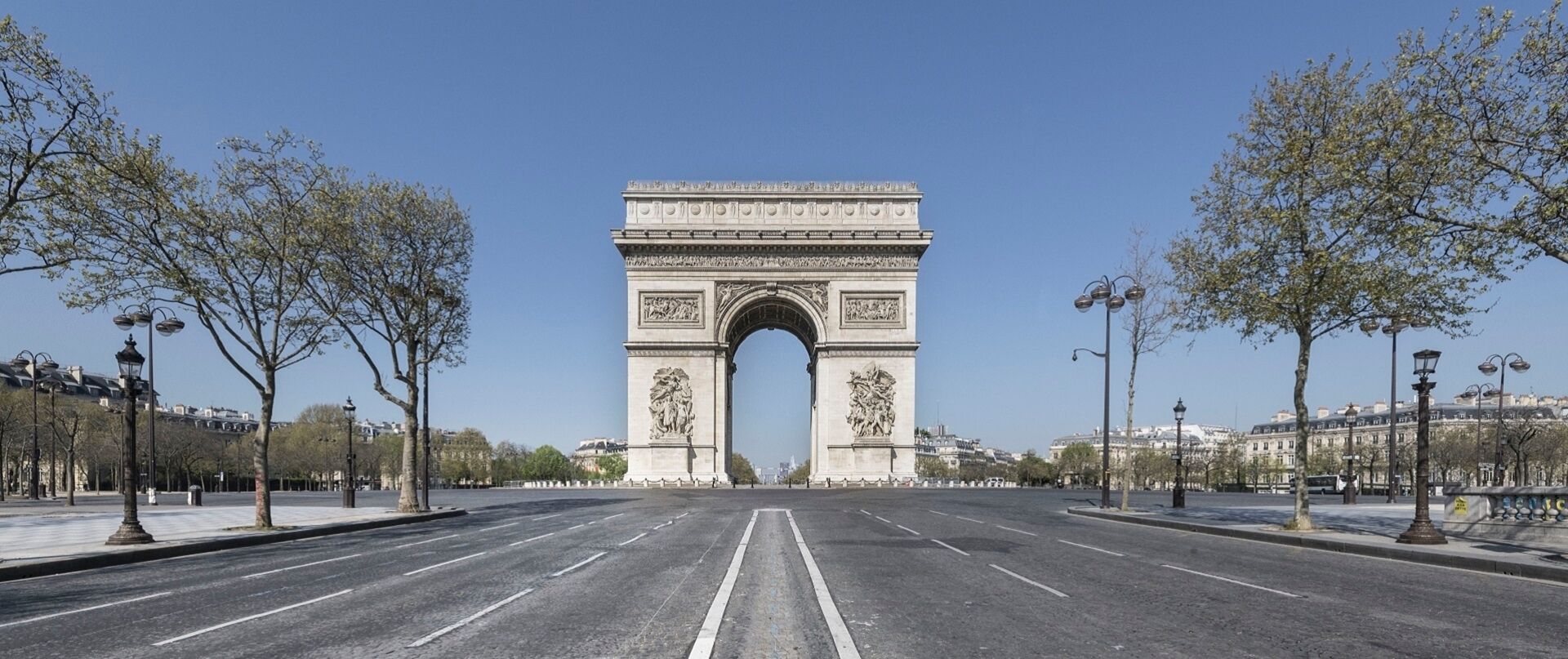 A wide, empty road leading to a large, ornate archway with classical sculptures.