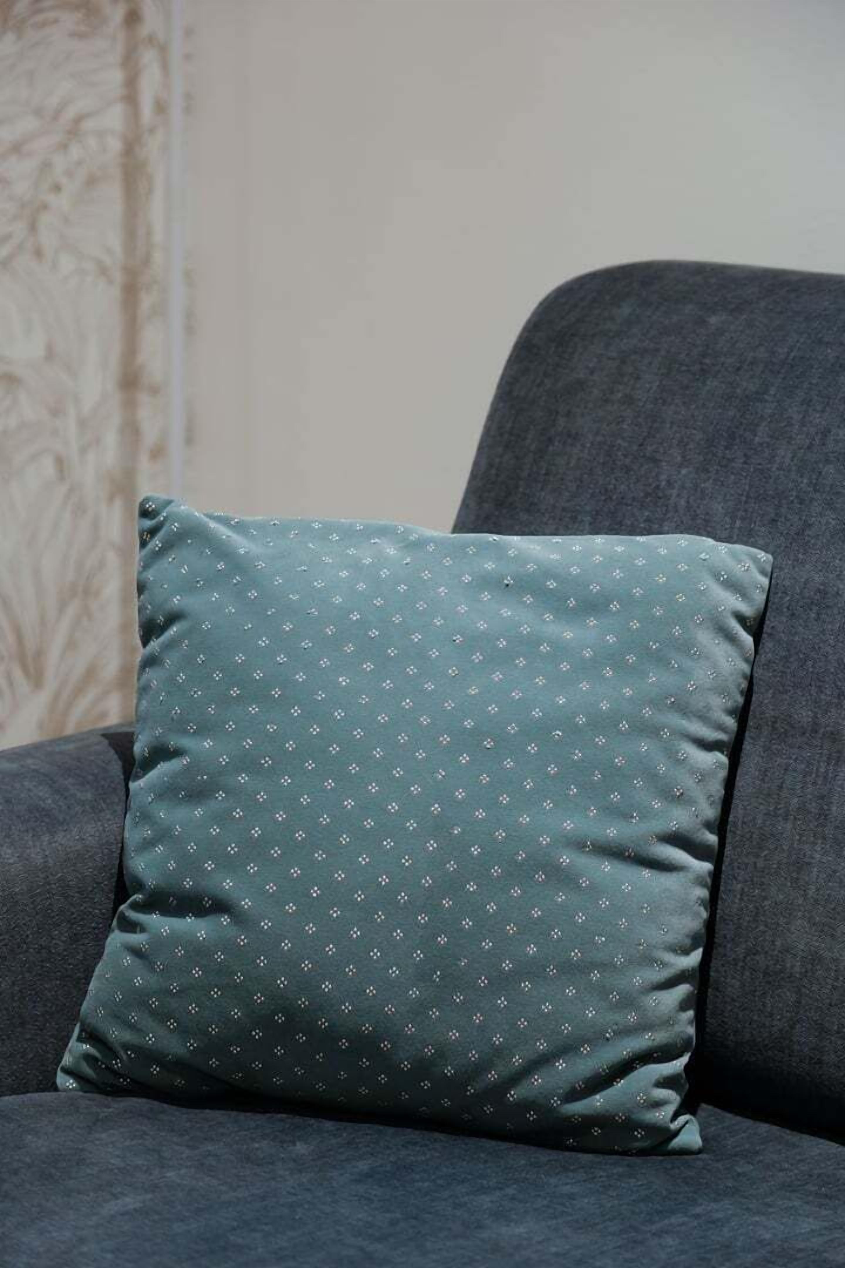 Un fauteuil de couleur gris foncé, agrémenté d’un coussin turquoise orné d’un petit motif blanc.