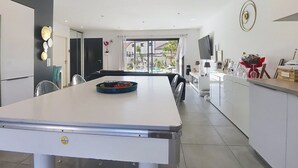 A modern kitchen with a dining area, a TV mounted on the wall, and a view of the outdoor pool. - Villa cami del paradis (Corneilla-del-Vercol)