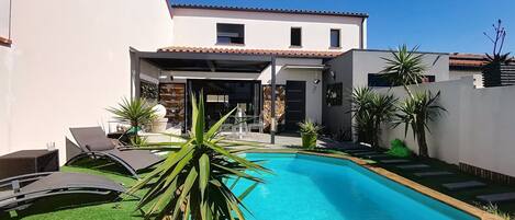 A modern house with a swimming pool, a covered patio, and a garden with various plants.