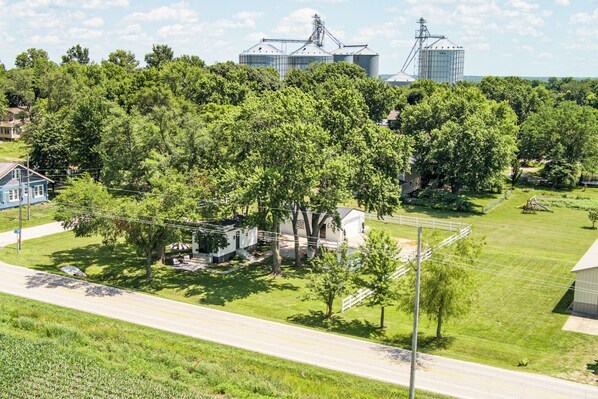 A rural landscape with a house surrounded by trees, a road, and grain silos in the background. - Cozy & Charming Cottage in Bucyrus (Bucyrus)
