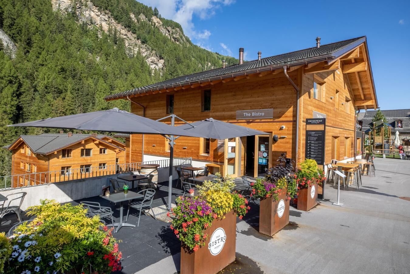 Una cabaña de madera con mobiliario exterior y macetas de flores, con la etiqueta “The Bistro”.
