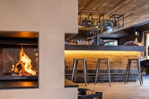 A bar area with a wooden ceiling, a fireplace, and bar stools.
