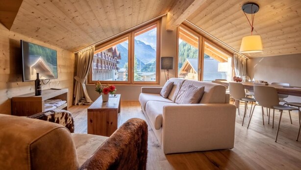 A spacious living area with a wooden ceiling, large windows offering mountain views, a sofa, a coffee table, and a dining table with chairs. - Wifi, resort center, tv, ski locker, 57-67m², Zinal (Zinal)