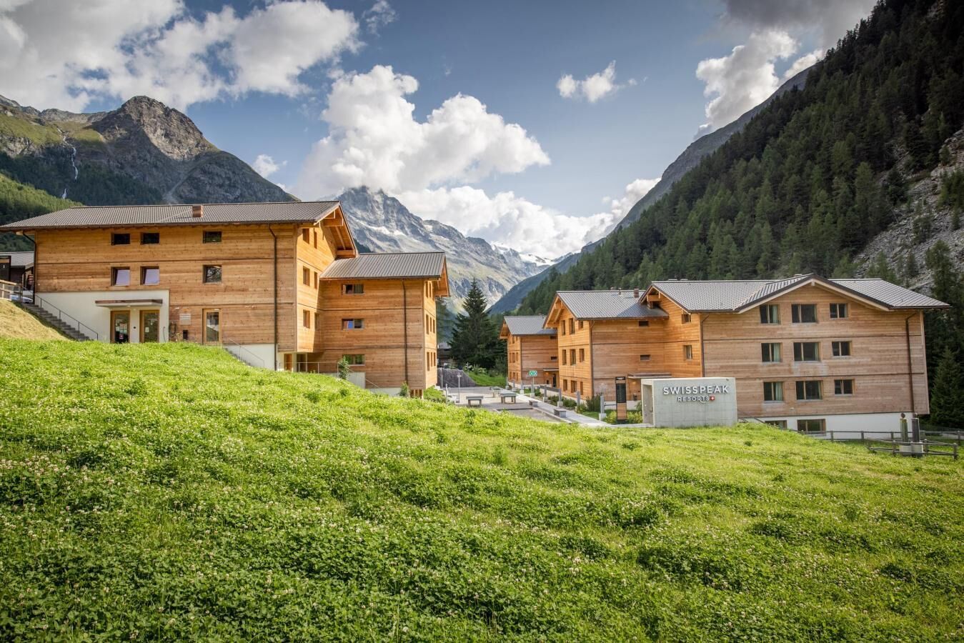 A wooden chalet-style building with multiple rooms, a sign reading "SWISSPEAK RESORT," and a mountainous backdrop.