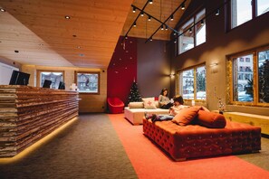 Un espace intérieur accueillant avec un comptoir d’accueil en bois, un coin salon avec des sièges rembourrés de couleur rouge et un sapin de Noël.