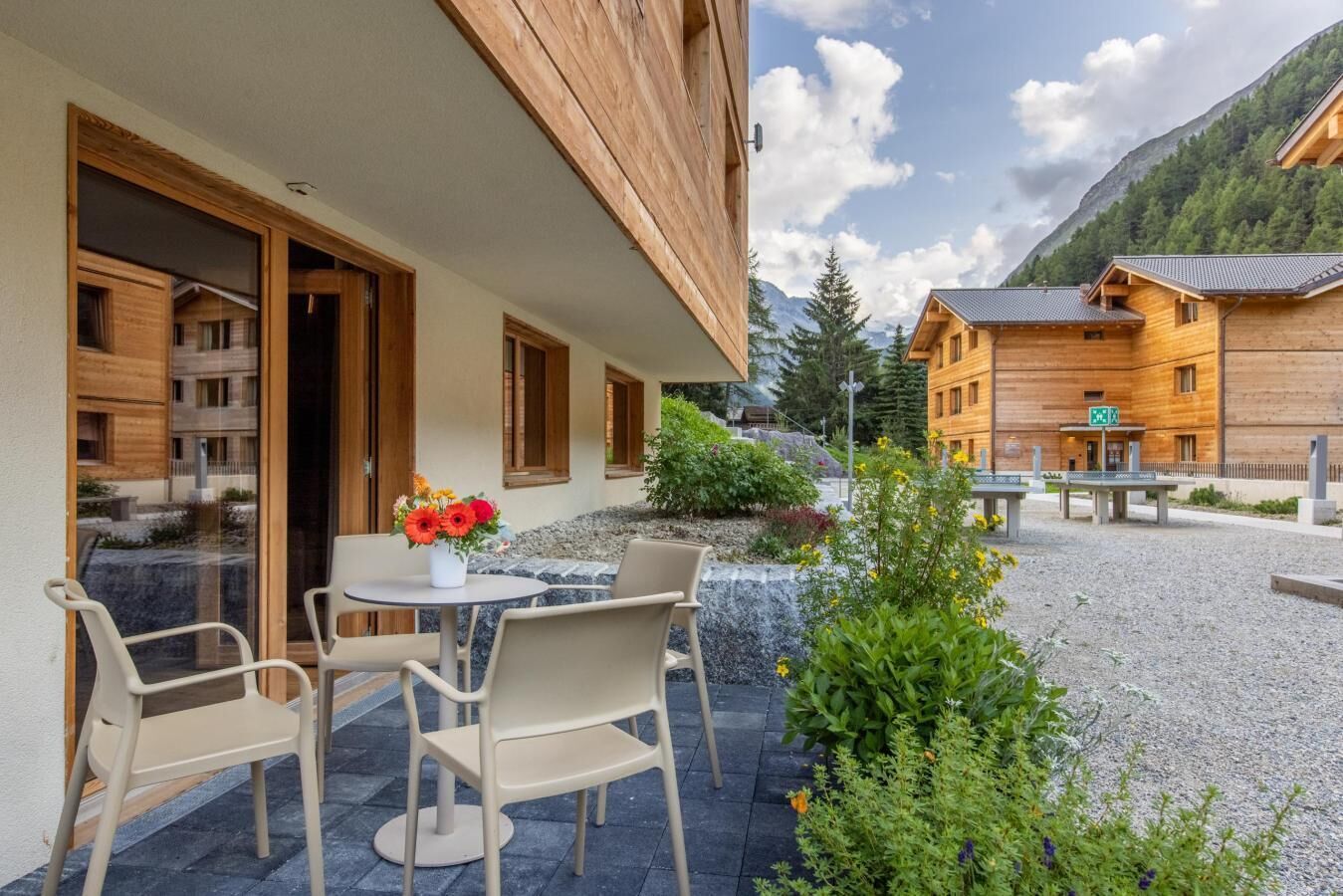 Un edificio de madera con balcón, mobiliario exterior y montañas al fondo.