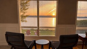 A room with two rocking chairs facing a large window with blinds, a small round table, and a view of a body of water. - La Brise O-Lac (Sherbrooke)