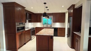 A modern kitchen with dark wood cabinets, stainless steel appliances, a granite countertop island, and pendant lighting.