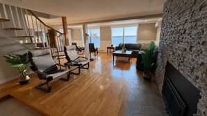 A spacious living room with a wooden floor, a stone accent wall, a fireplace, and a view of the sea. - La Brise O-Lac (Sherbrooke)